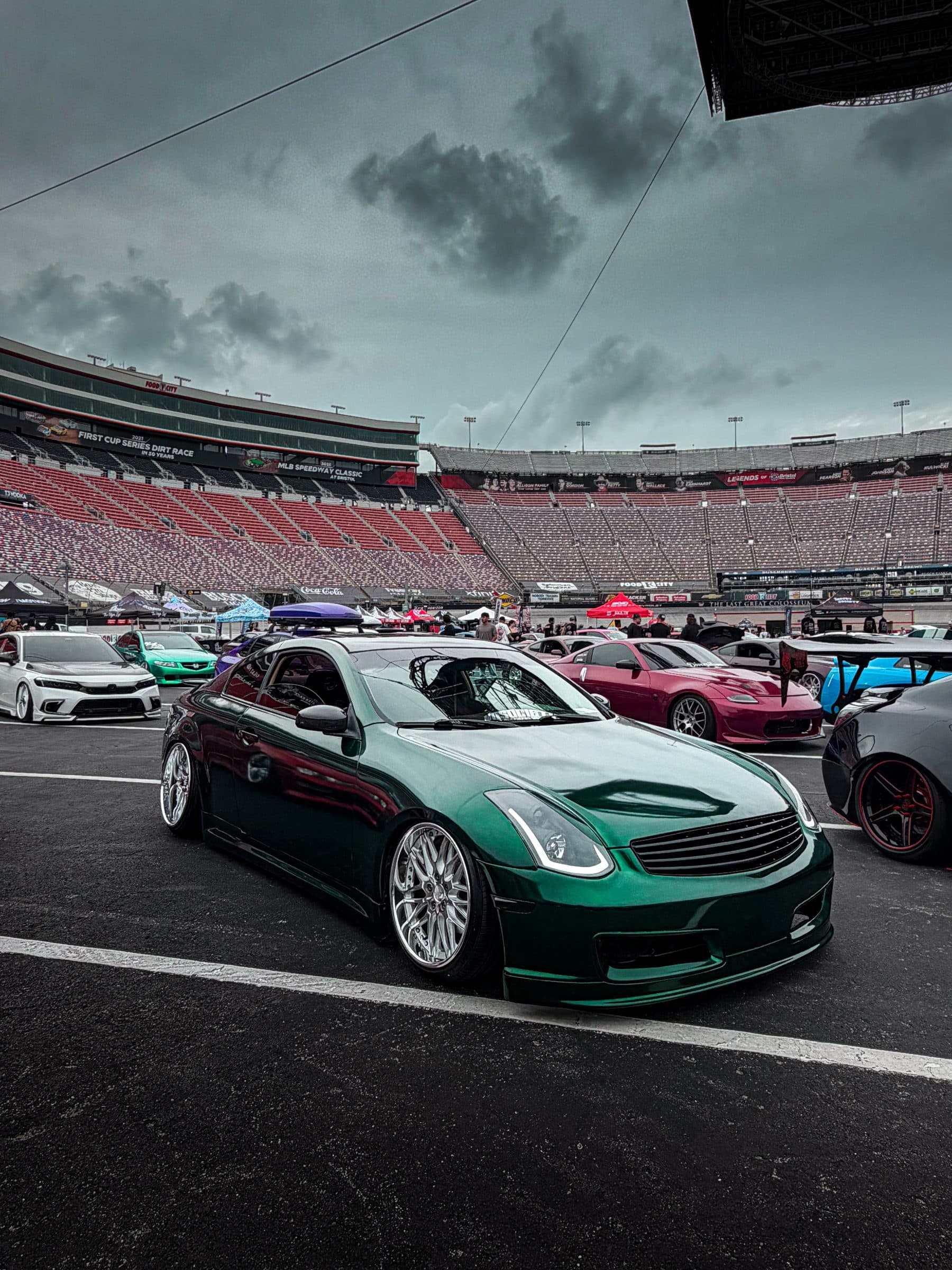 Aidan's green Infiniti G35 at a car meet in front of racetrack grandstands