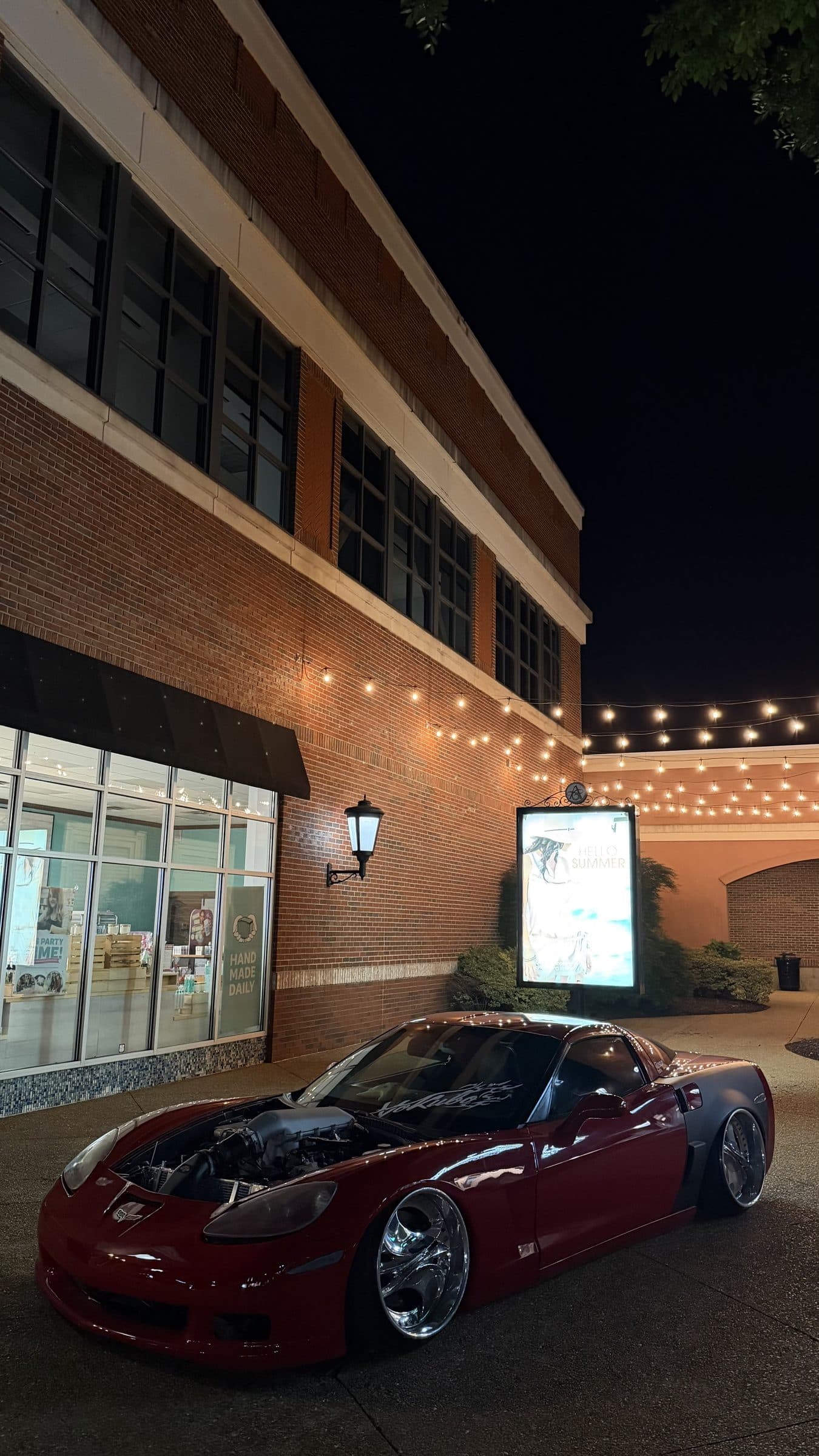 Clayton's red C6 Corvette beside a brick building strung with lights at night