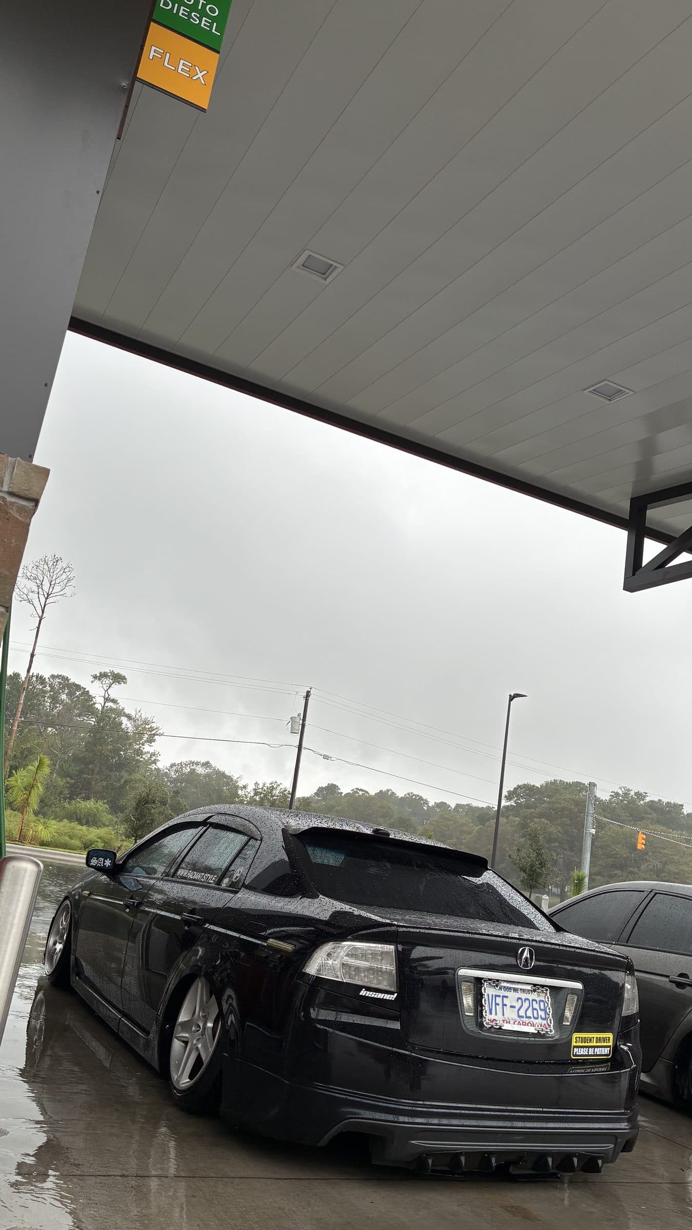 Rear three-quarter view of Jonah's black Acura TL under a fuel-station canopy