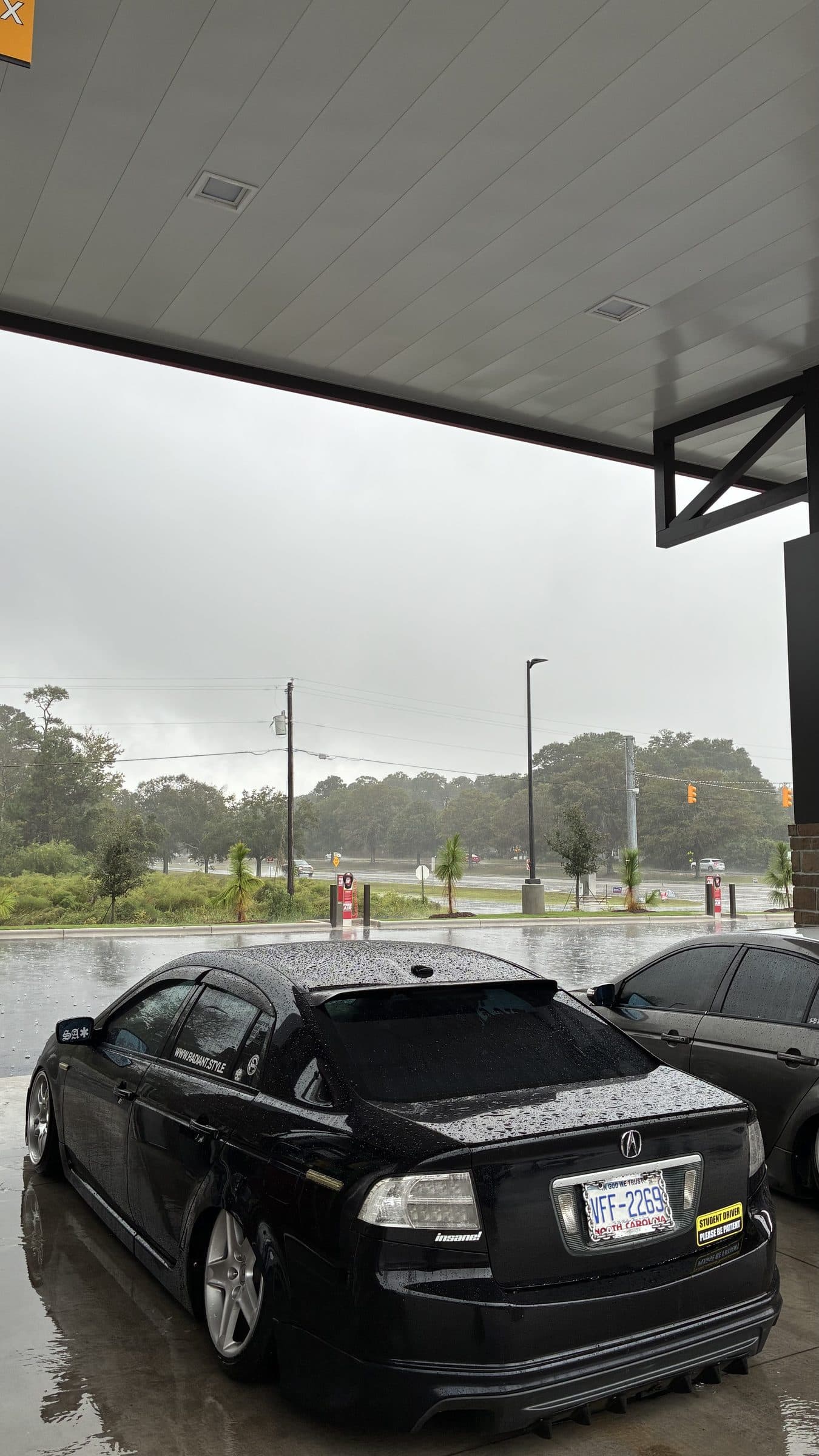 Jonah's rain-soaked black Acura TL parked under a fuel-station canopy