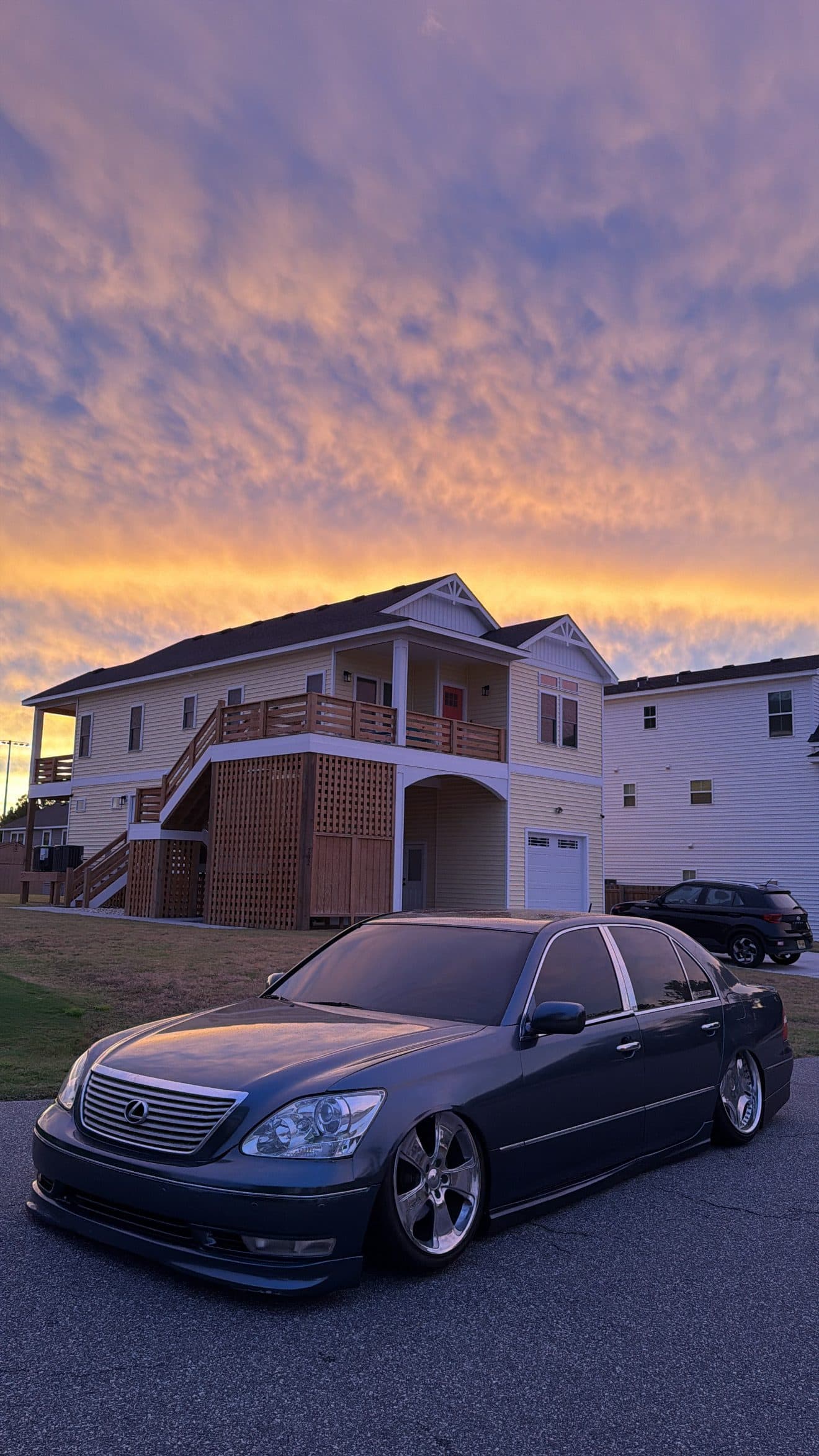 Front three-quarter view of Juan's grey Lexus LS430 under a pink and orange sky