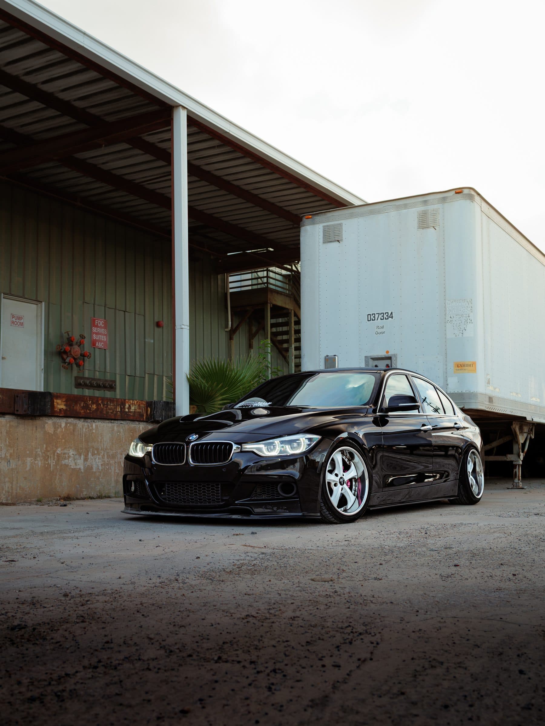 Keller's black BMW F30 beside a trailer at a loading dock