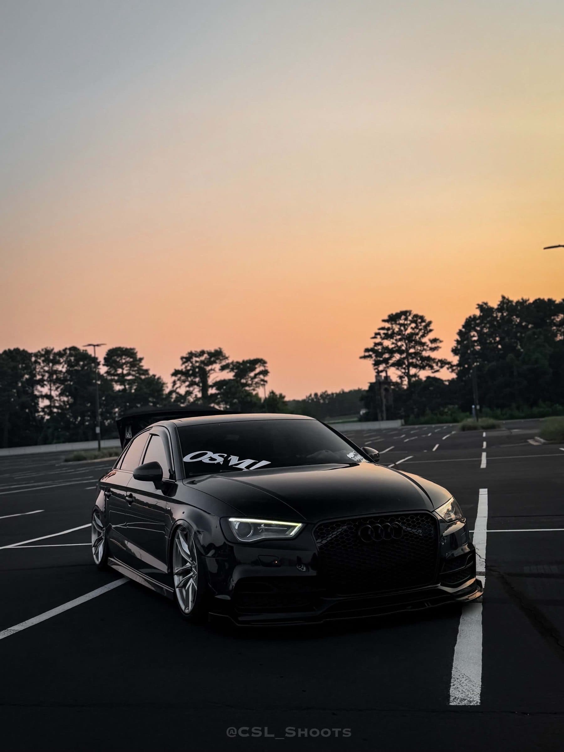 Tristan's black Audi A3 head-on in an empty lot at sunset