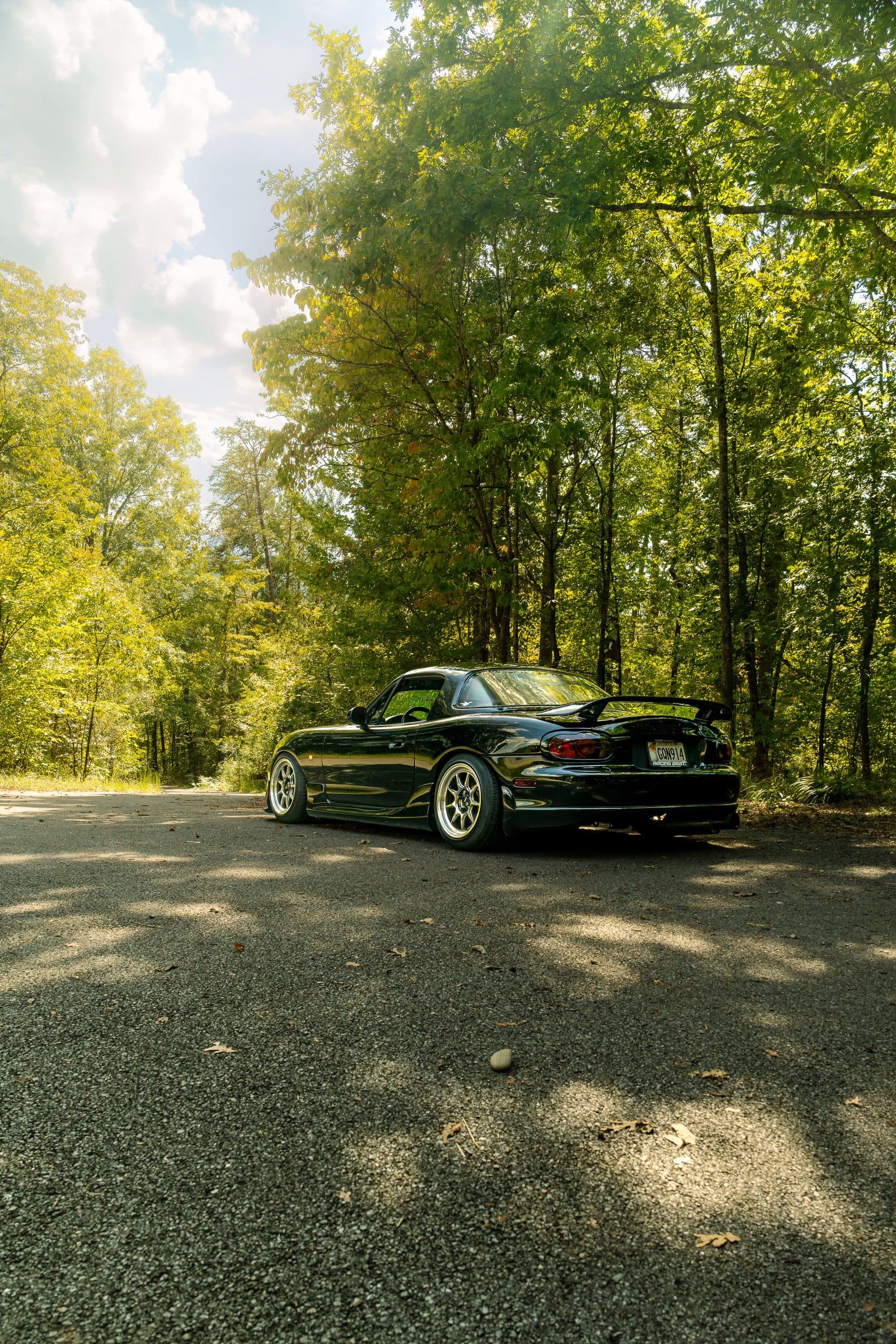 Stephen's black NB Miata on a tree-lined road, seen from behind